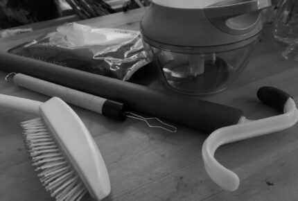 Black and white image of aids including small veg chopper, long handled hairbrush, and a large dressing stick and small button hole dressing tool.