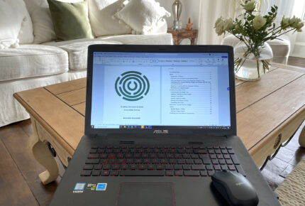 Image showing laptop on table ion a living room. Sofa and plants in the background. The laptops screen shows a Disability Information Scotland training page.