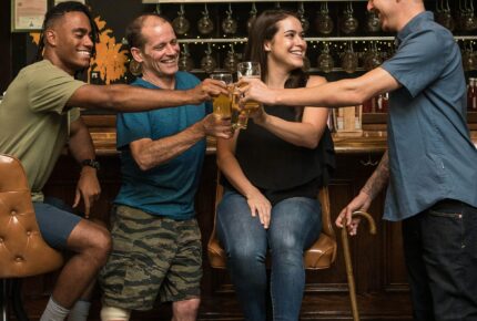 Four people clinking glasses. One has a leg prosthesus and one a walking stick.