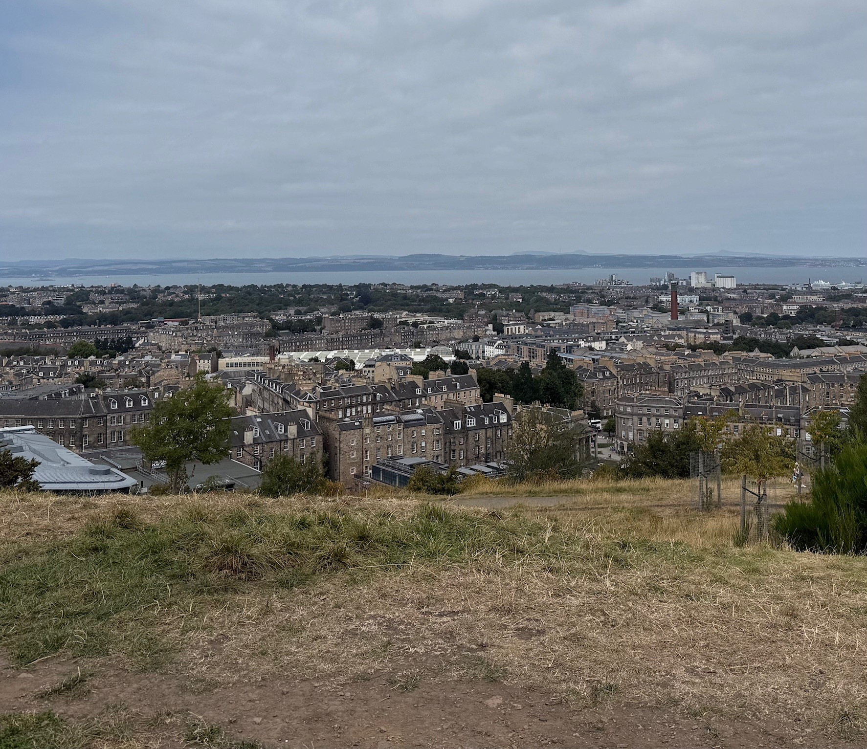 Grass in foreground and view over Edinburgh with the River Forth in the distance and the landmass of Fife.