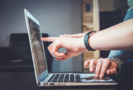 a finger pointing towards a laptop screen with another hand using the laptop touchpad
